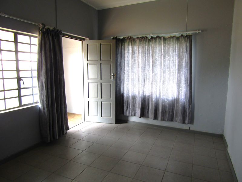 An empty bedroom featuring tiled flooring, a steel-framed window, and a panel door, offering a blank canvas for renovation.