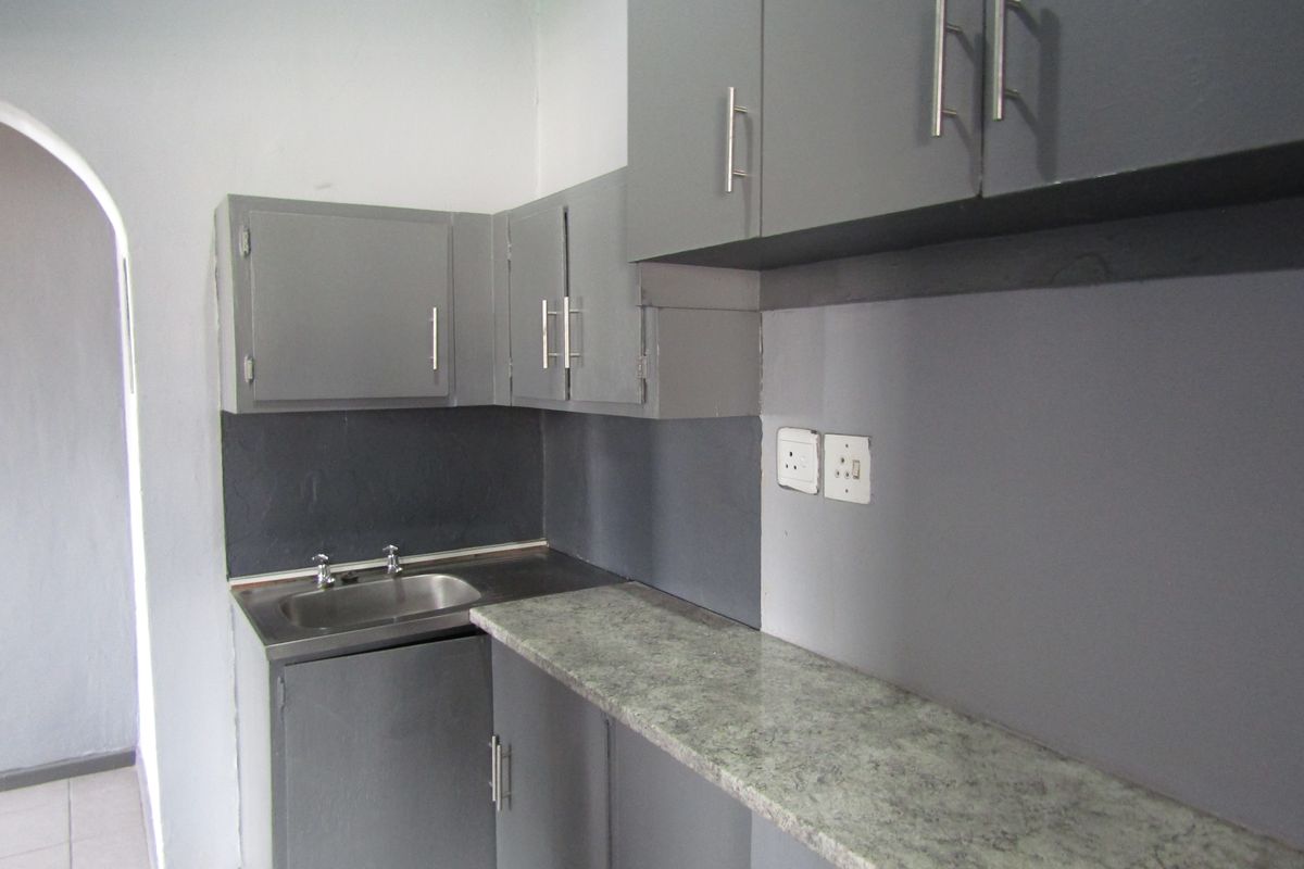 A compact kitchen area featuring grey painted built-in cabinetry, a laminate countertop, and a stainless steel sink with an arched entryway.