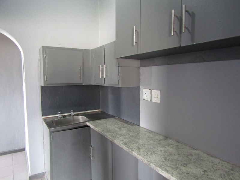 A compact kitchen area featuring grey painted built-in cabinetry, a laminate countertop, and a stainless steel sink with an arched entryway.