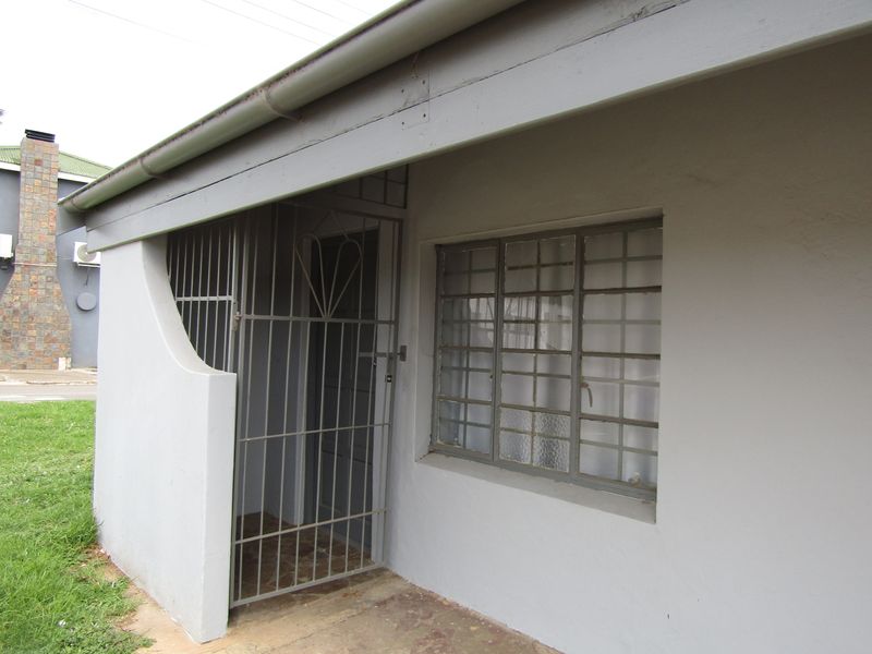 Front entrance area of the flat featuring a security gate, protective window bars, and a concrete pathway.