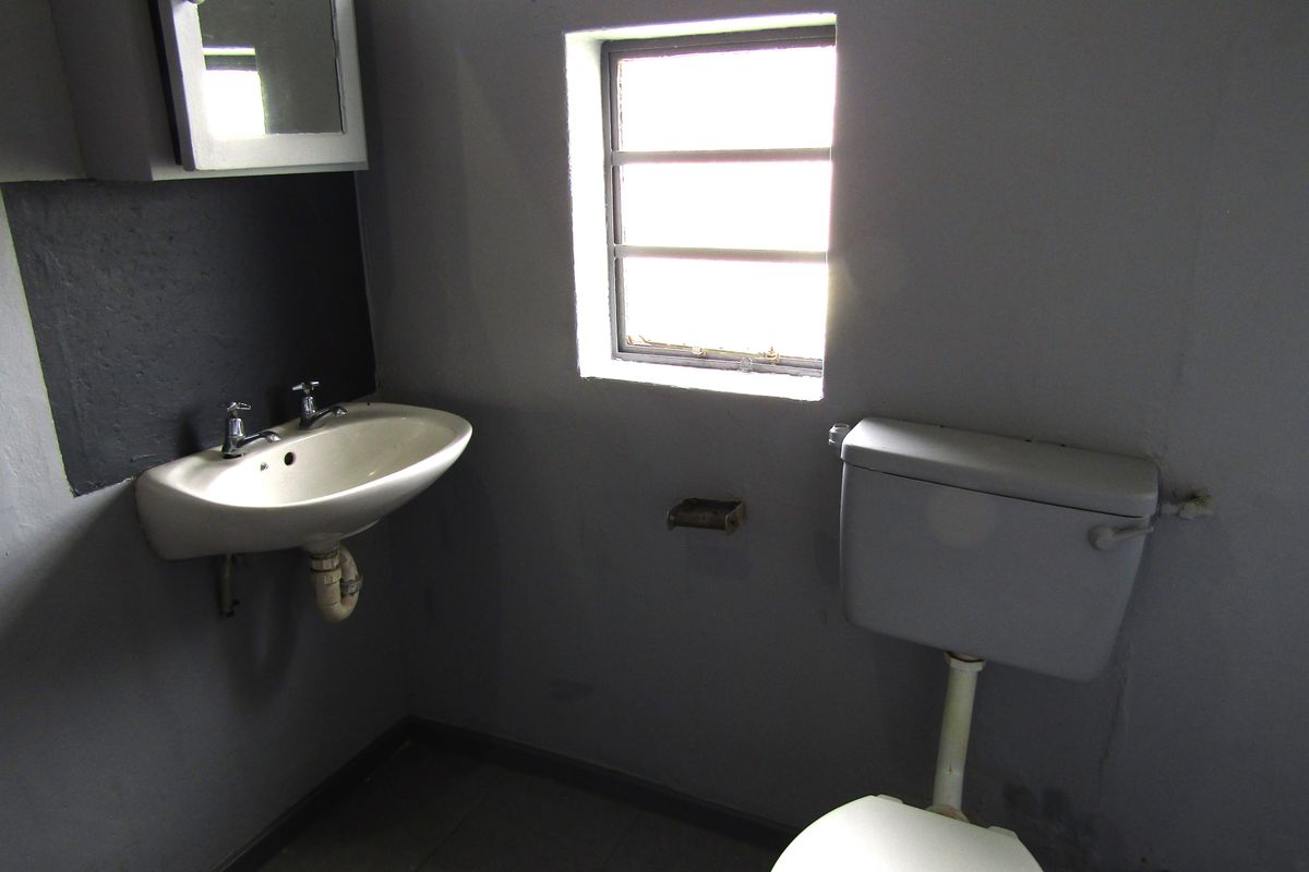 A compact bathroom featuring a wall-mounted basin, toilet, and medicine cabinet, requiring cosmetic updates to improve the overall aesthetic and condition.