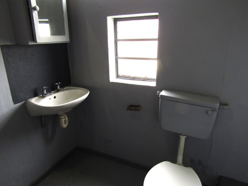 A compact bathroom featuring a wall-mounted basin, toilet, and medicine cabinet, requiring cosmetic updates to improve the overall aesthetic and condition.