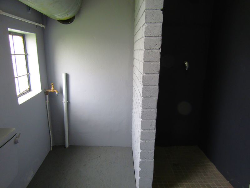 A basic, unfinished bathroom space featuring a shower area, exposed plumbing, and a small window, offering potential for a complete modern renovation.