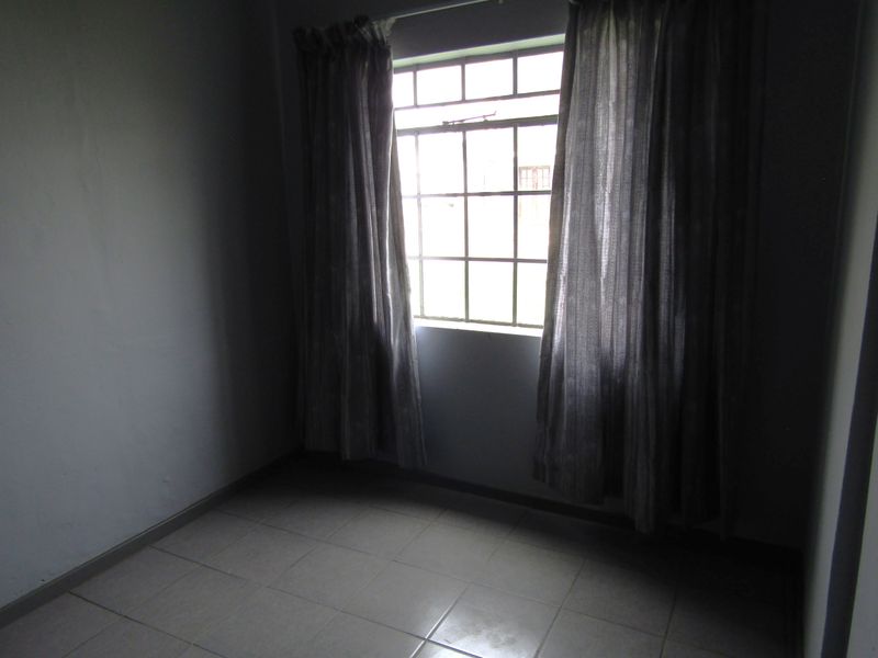 An empty bedroom featuring tiled flooring and a grid-pattern window, providing a blank canvas for personalization.