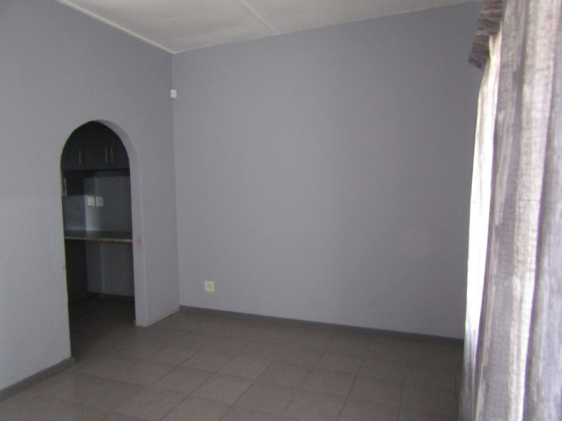 An empty living room featuring neutral grey walls, tiled flooring, and an arched entryway leading to an adjacent kitchen area.