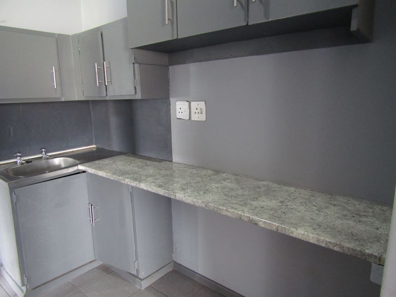 A compact kitchen area featuring grey built-in cabinetry, a laminate countertop, and a stainless steel sink.