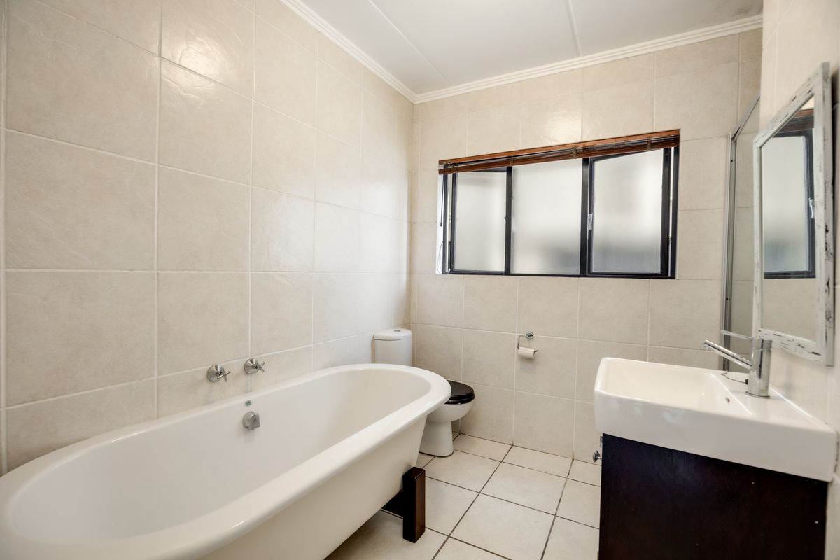 A functional bathroom featuring a freestanding bathtub, a wall-mounted vanity basin, and a toilet, finished with neutral wall and floor tiling.