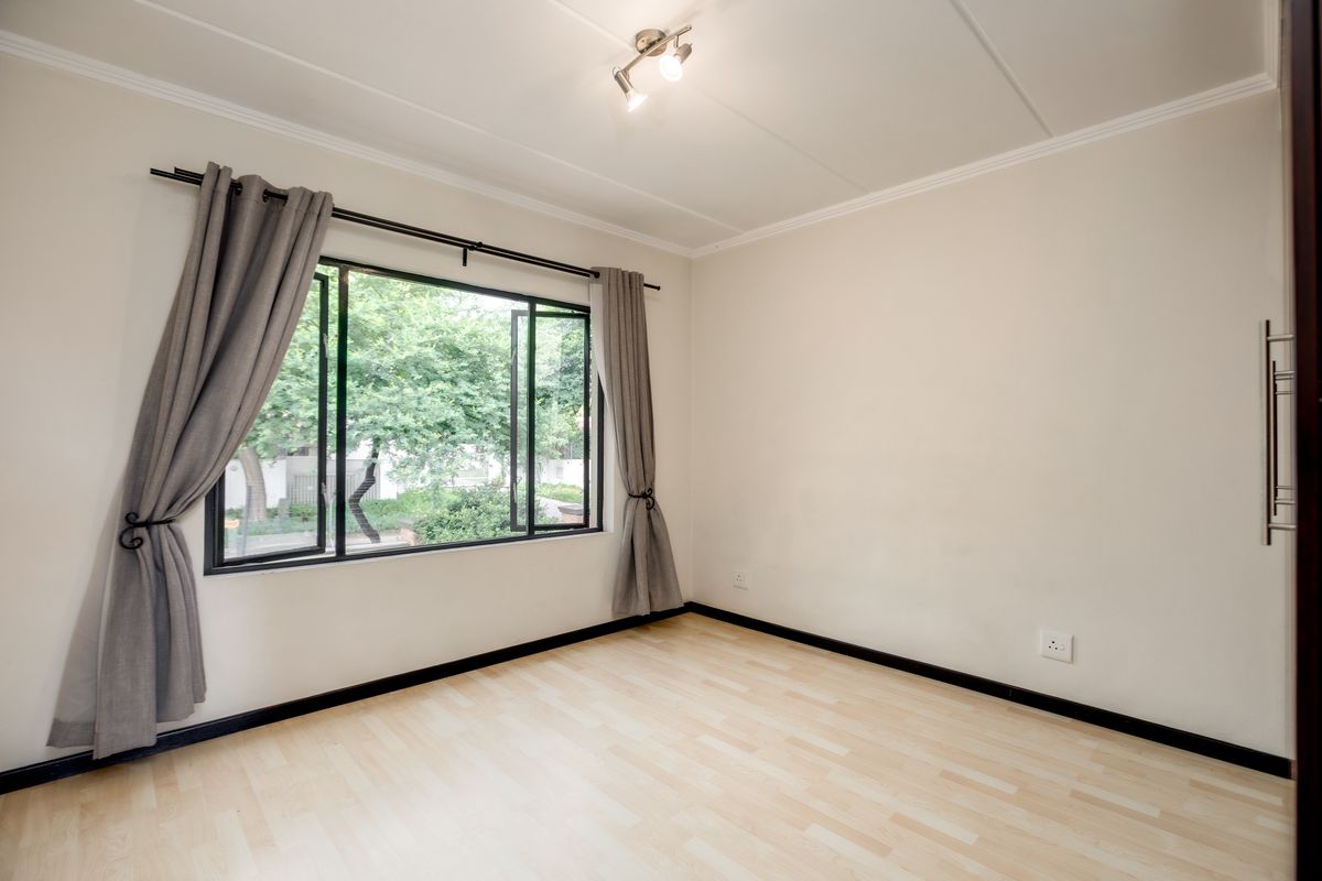 A bright, empty bedroom featuring light wood-look flooring, neutral walls, and a large window with garden views.