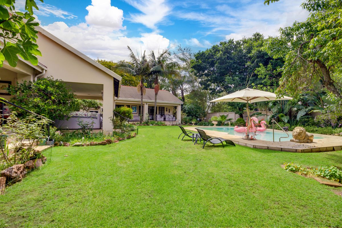 Spacious rear garden featuring a well-maintained lawn, a swimming pool with paved surround, and a covered patio area for outdoor entertaining.