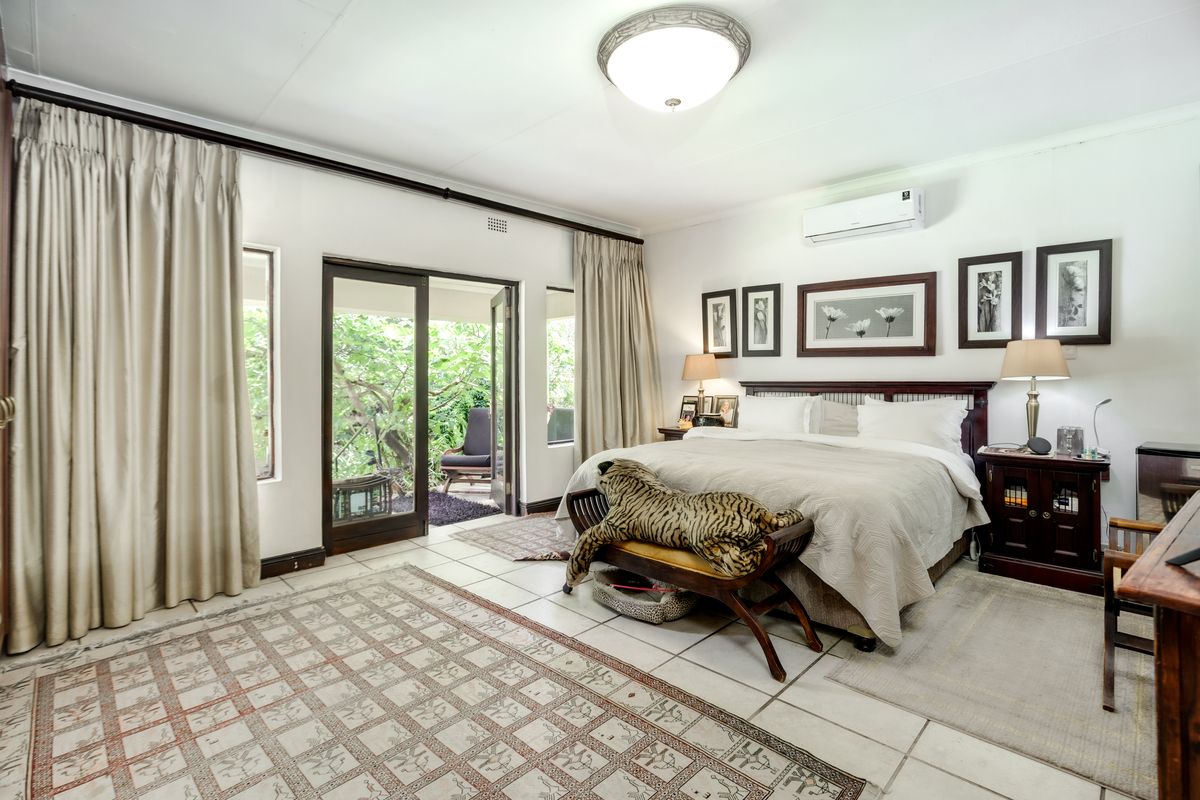 Spacious bedroom featuring tiled flooring, a wall-mounted air conditioning unit, and direct access to a private patio through sliding glass doors.