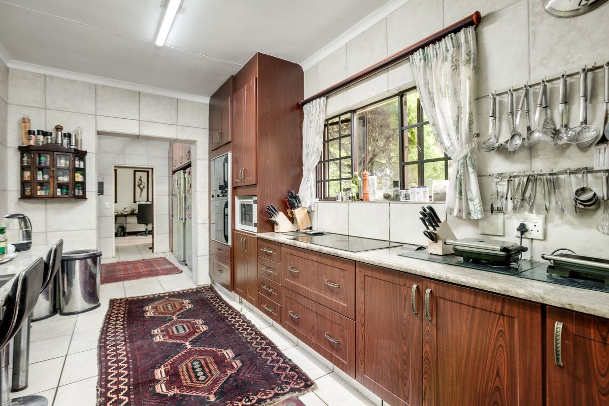 A functional kitchen featuring dark wood cabinetry, stone-look countertops, tiled walls, and a built-in oven, with a view through to an adjacent room.
