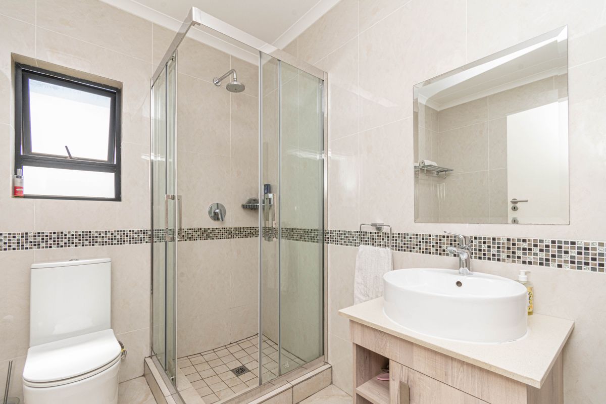 Modern bathroom featuring a glass-enclosed shower, a contemporary vessel sink vanity, and neutral wall tiling with a decorative mosaic accent border.
