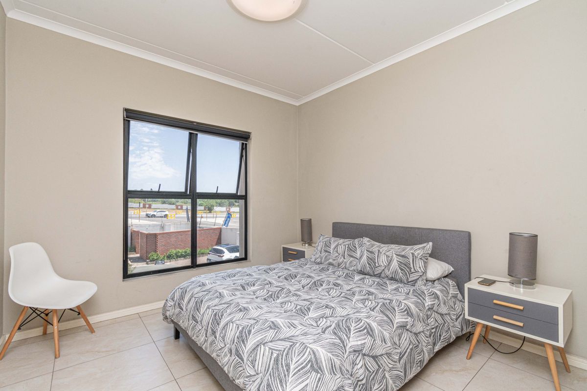A well-lit bedroom featuring neutral wall tones, tiled flooring, and a large window providing natural light and exterior views.