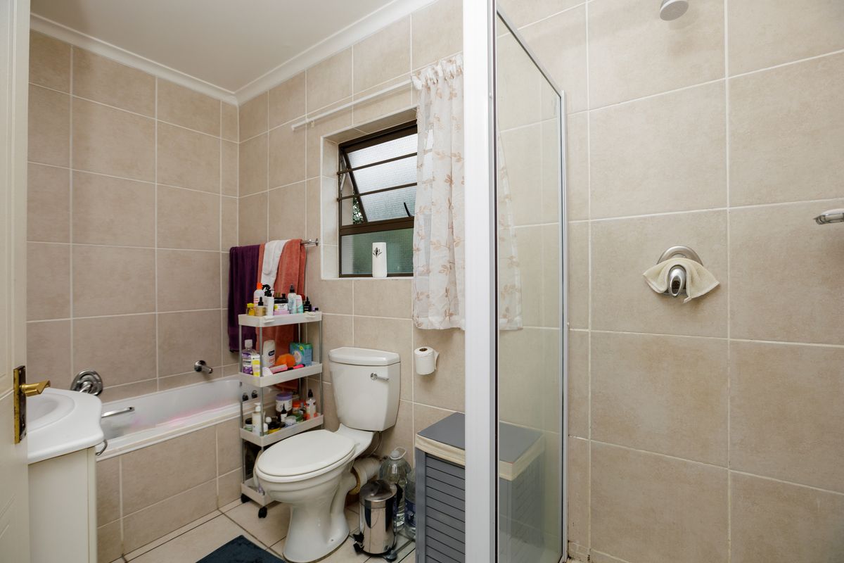 A functional bathroom featuring a built-in bathtub, separate glass-enclosed shower, toilet, and vanity basin with neutral wall and floor tiling.