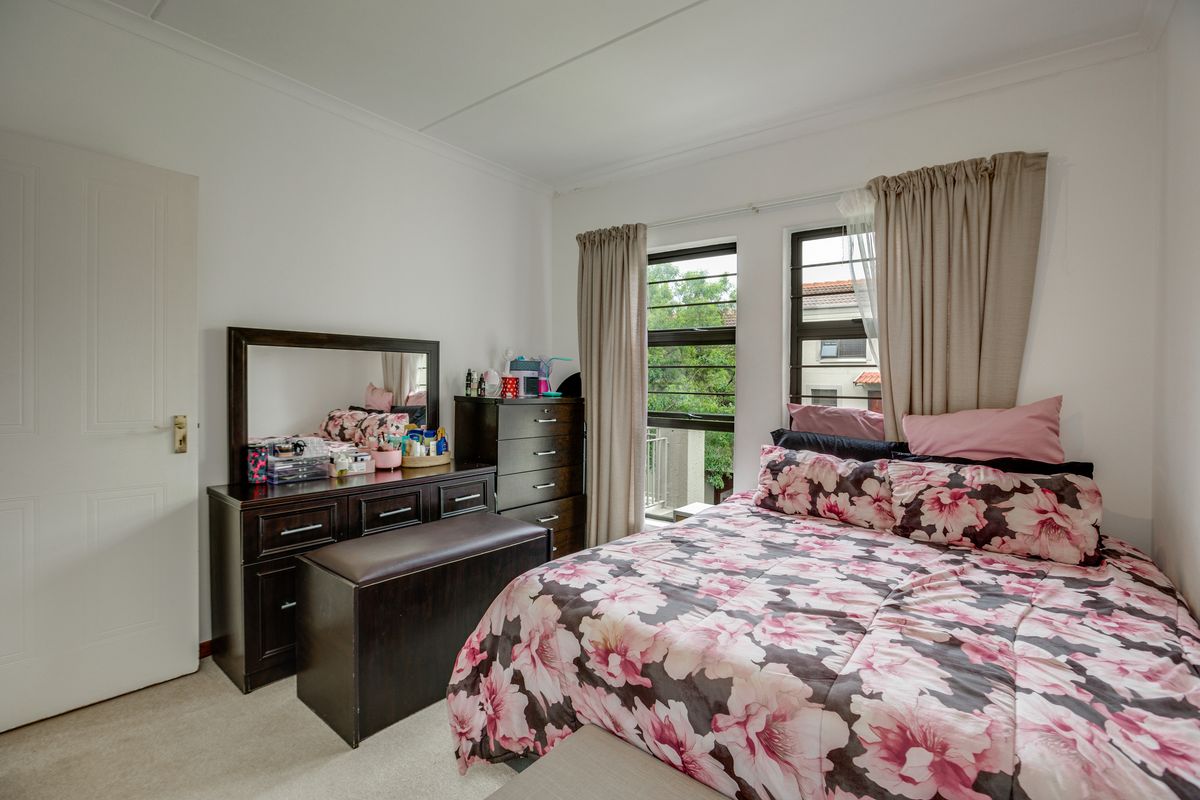 A well-lit bedroom featuring neutral carpeting, white walls, and large windows with security bars, providing natural light and ventilation.