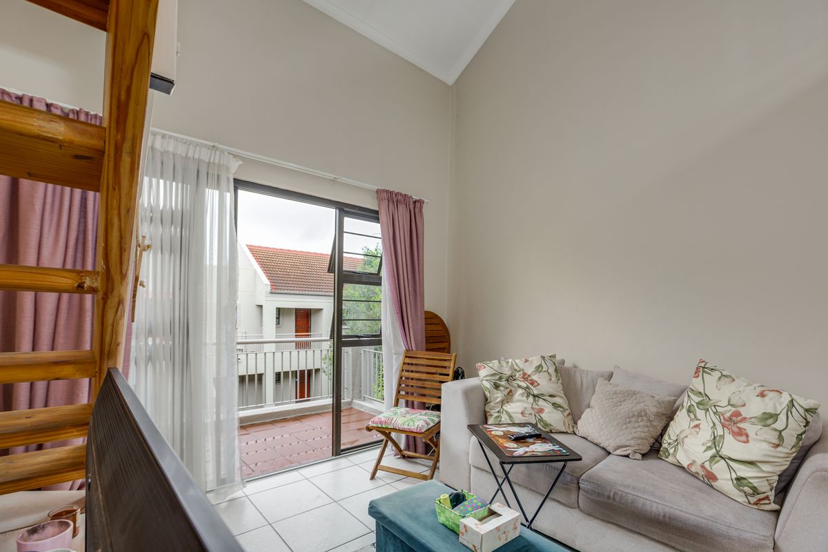 A bright living room featuring high vaulted ceilings, tiled flooring, and large sliding glass doors that open onto a private balcony.
