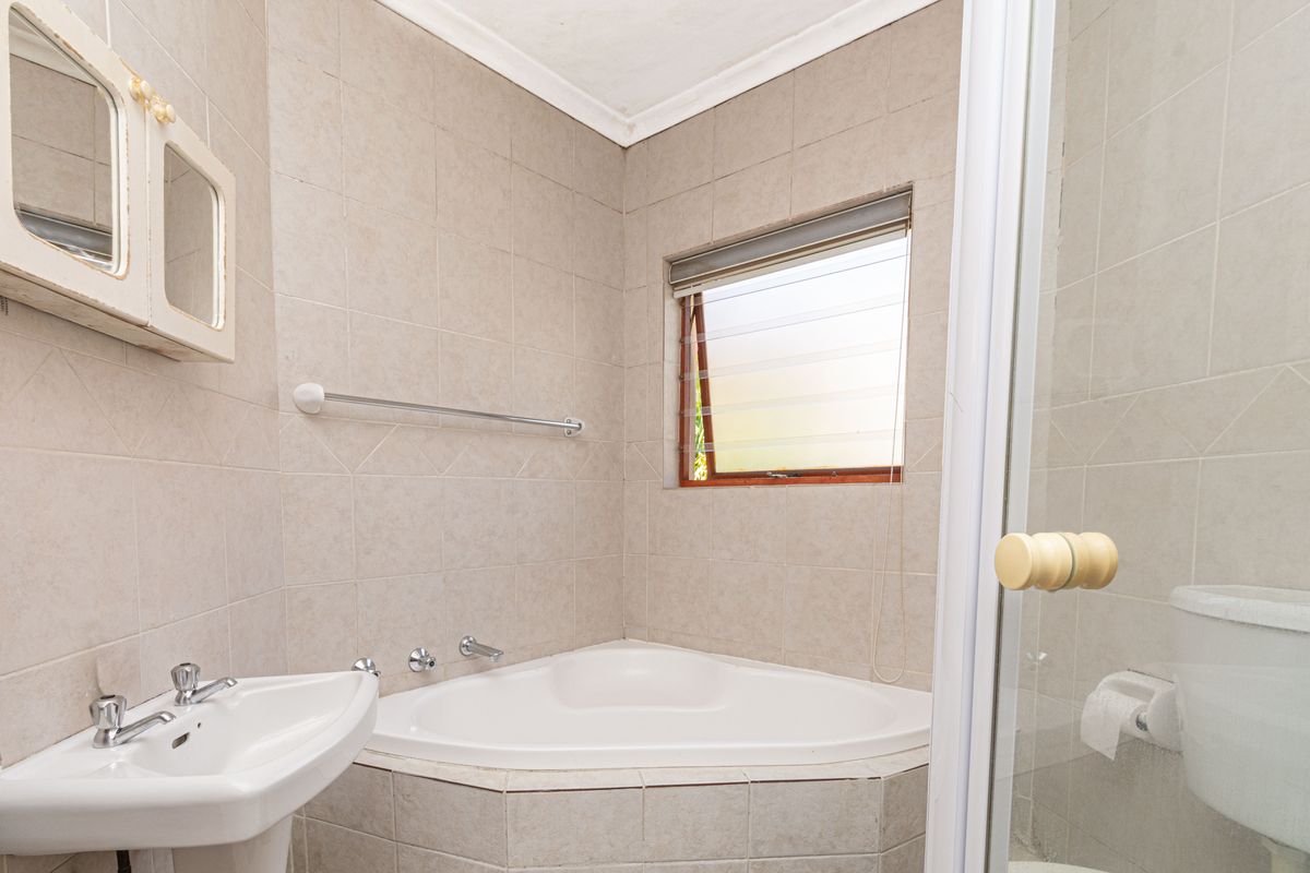 A functional bathroom featuring a corner bathtub, pedestal basin, and tiled walls, offering a practical layout for daily use.