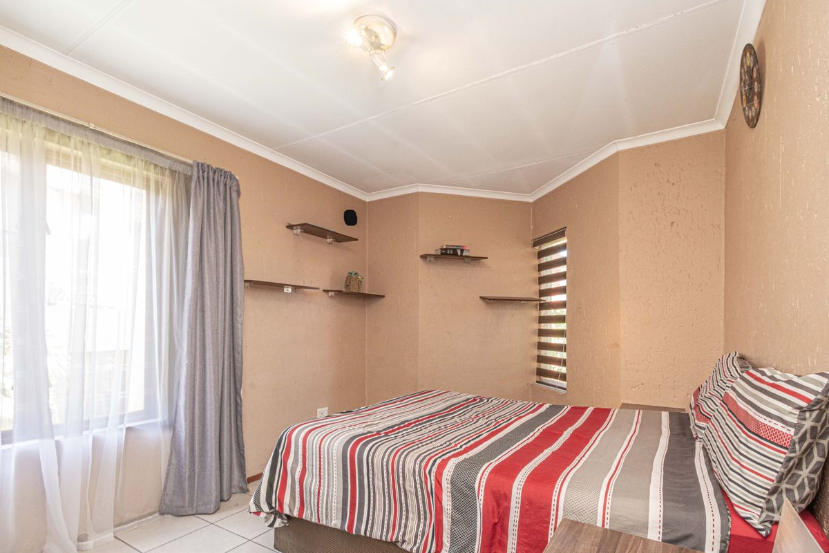 A bedroom featuring textured walls, tiled flooring, and built-in wall shelving, offering a functional space with natural light from the window.