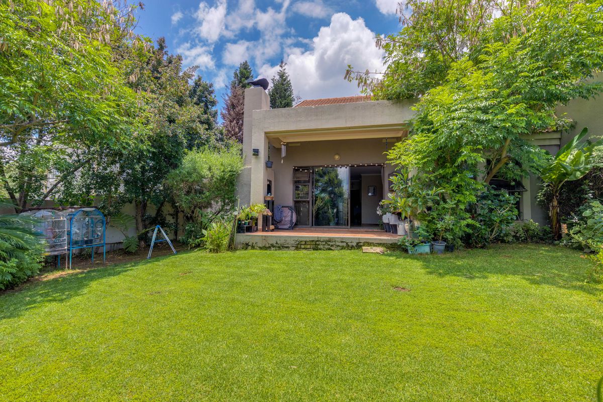 Rear view of the townhouse featuring a covered patio with a built-in braai, sliding glass doors, and a well-maintained private garden.