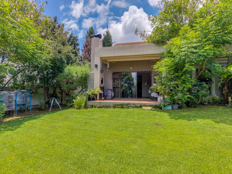 Rear view of the townhouse featuring a covered patio with a built-in braai, sliding glass doors, and a well-maintained private garden.