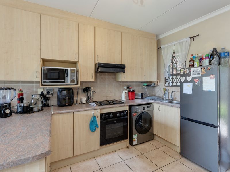 Functional kitchen featuring light wood-finish cabinetry, laminate countertops, built-in oven, hob, extractor fan, and integrated microwave with tiled flooring and backsplash.