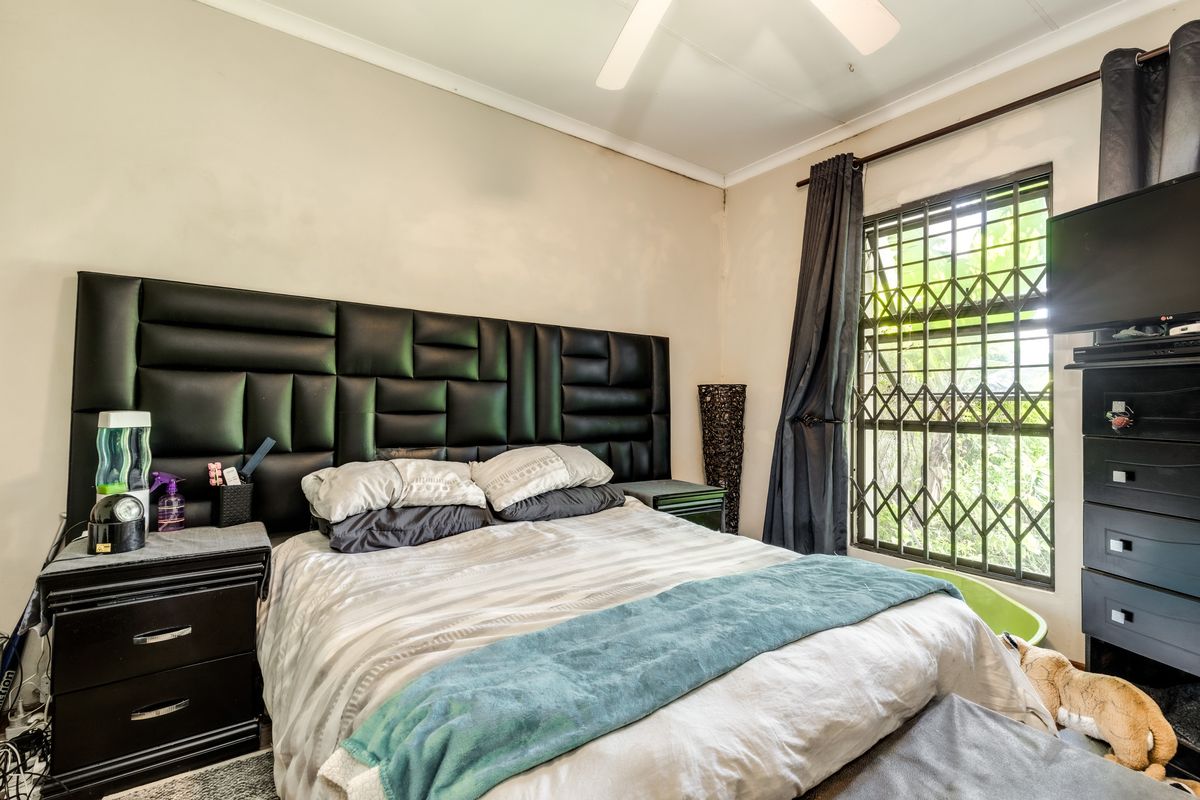 A bedroom featuring a ceiling fan and a window fitted with a security gate, showing signs of wear on the wall surfaces.