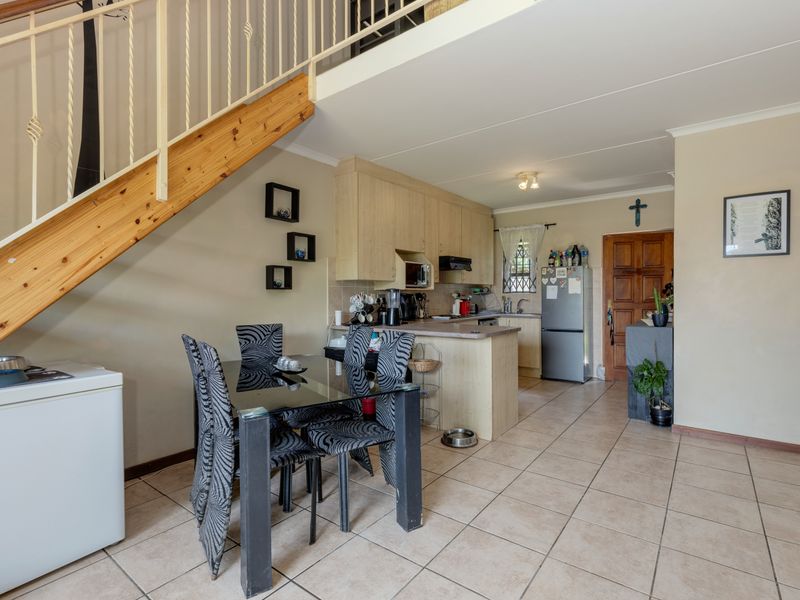 Open-plan kitchen and dining area featuring tiled flooring, wooden staircase with metal balustrade, and functional kitchen cabinetry.
