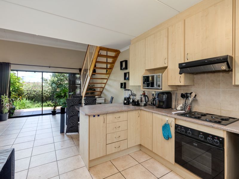 Open-plan kitchen and living area featuring light wood cabinetry, built-in appliances, tiled flooring, and direct access to the rear patio via sliding glass doors.