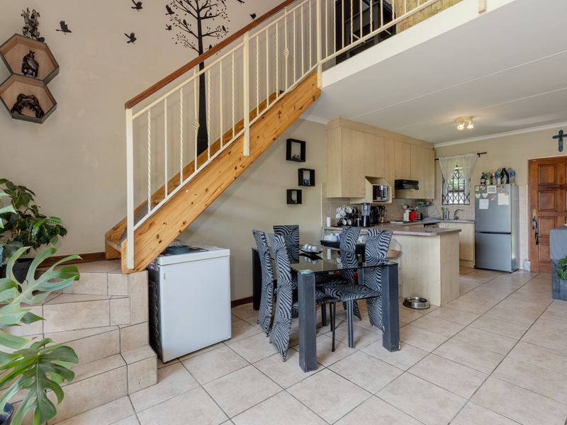 Open-plan living area featuring a staircase, tiled flooring, and a functional kitchen with built-in cabinetry and an extractor fan.