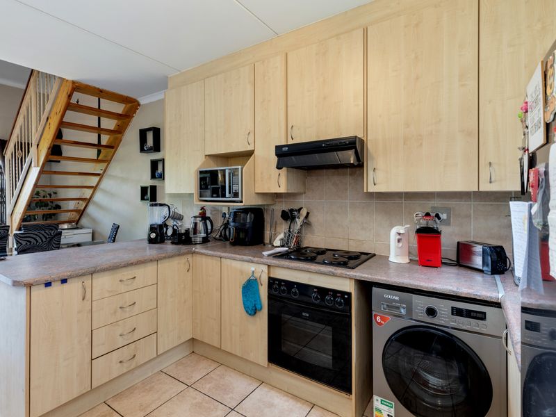 Functional kitchen featuring light wood-finish cabinetry, laminate countertops, built-in oven, hob, and extractor fan, with an adjacent staircase leading to the upper level.