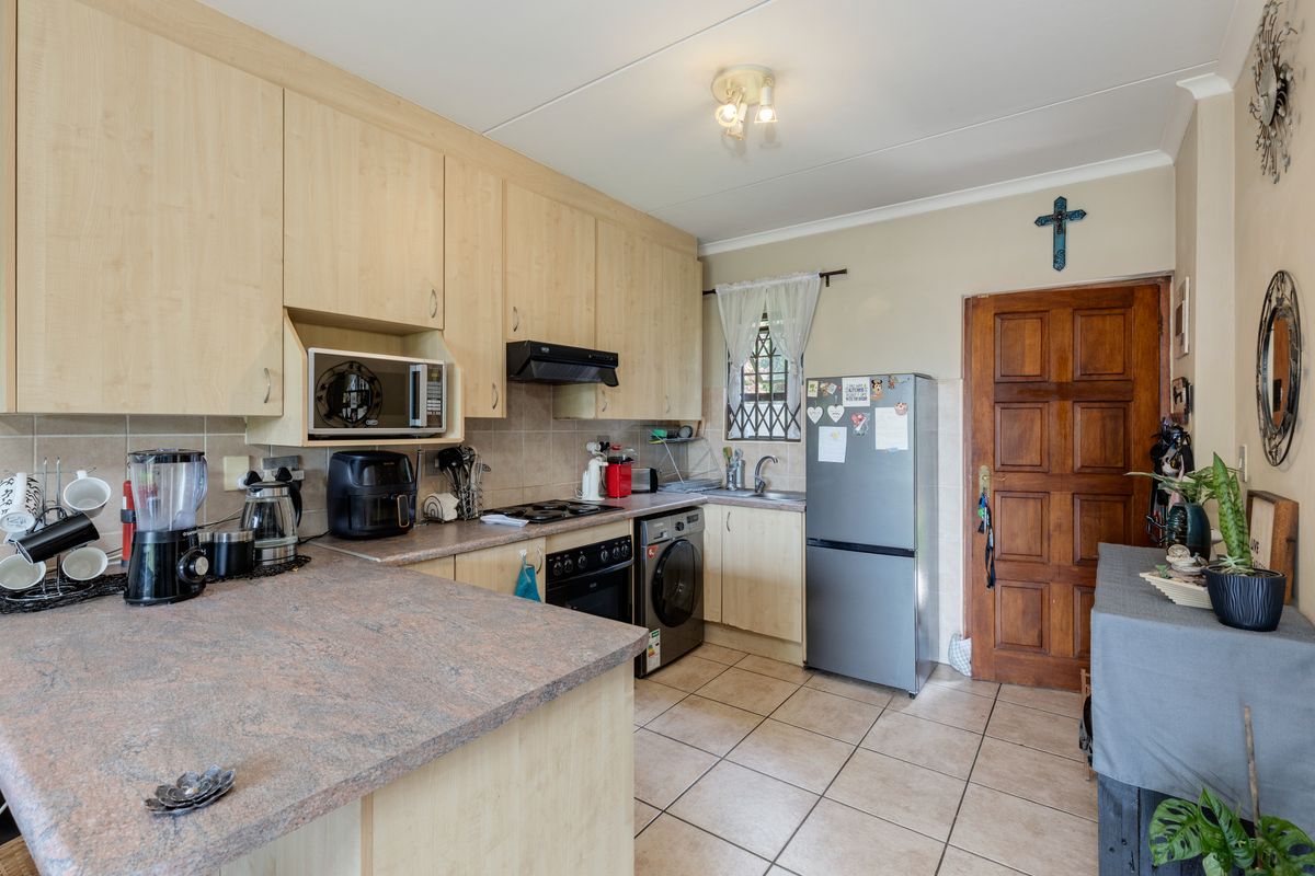 Functional kitchen featuring light wood-finish cabinetry, stone-look laminate countertops, built-in oven with extractor, and tiled flooring with a classic wooden door entrance.