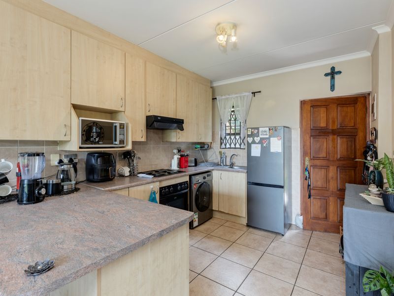 Functional kitchen featuring light wood-finish cabinetry, stone-look laminate countertops, built-in oven with extractor, and tiled flooring with a classic wooden door entrance.