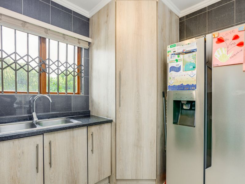 A functional kitchen area featuring light wood-finish cabinetry, dark granite countertops, a double sink, and tiled wall finishes.