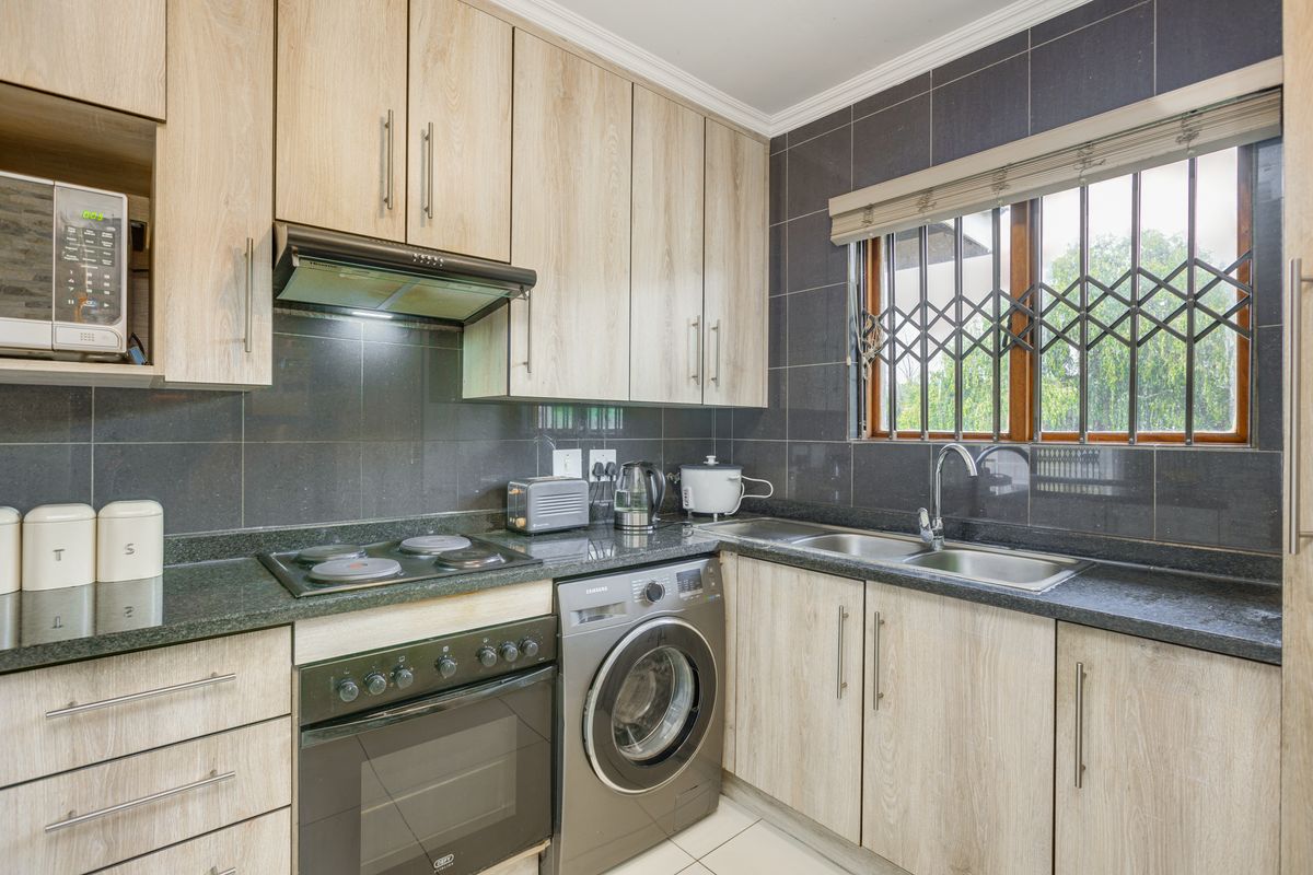 A well-maintained kitchen featuring light wood-finish cabinetry, dark granite countertops, a built-in oven, hob, extractor fan, and integrated washing machine.
