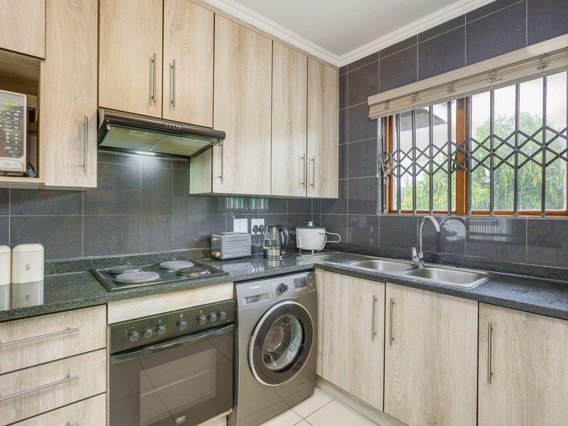 A well-maintained kitchen featuring light wood-finish cabinetry, dark granite countertops, a built-in oven, hob, extractor fan, and integrated washing machine.