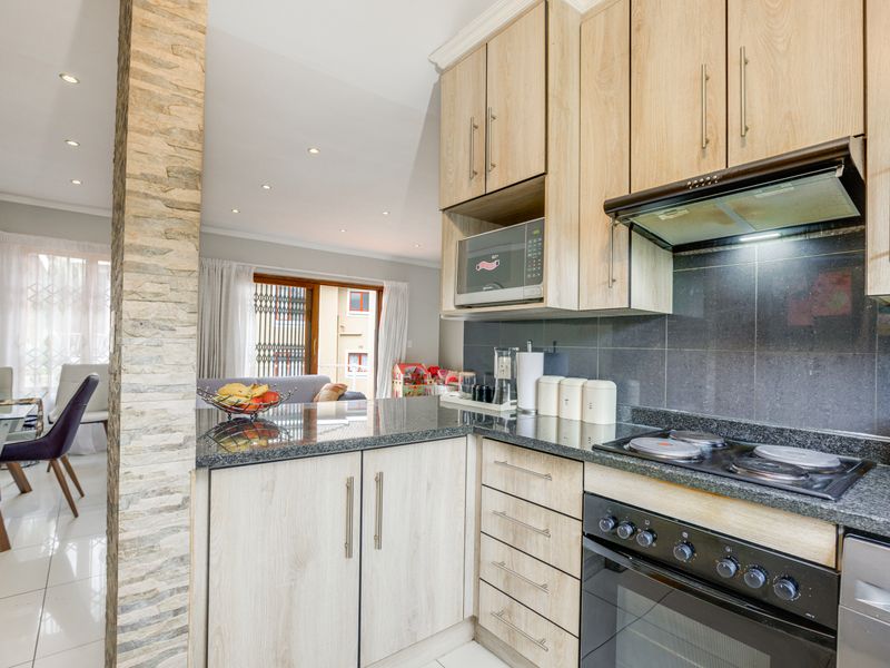 Modern open-plan kitchen featuring light wood cabinetry, granite countertops, and integrated appliances, seamlessly flowing into the adjacent dining and living area.