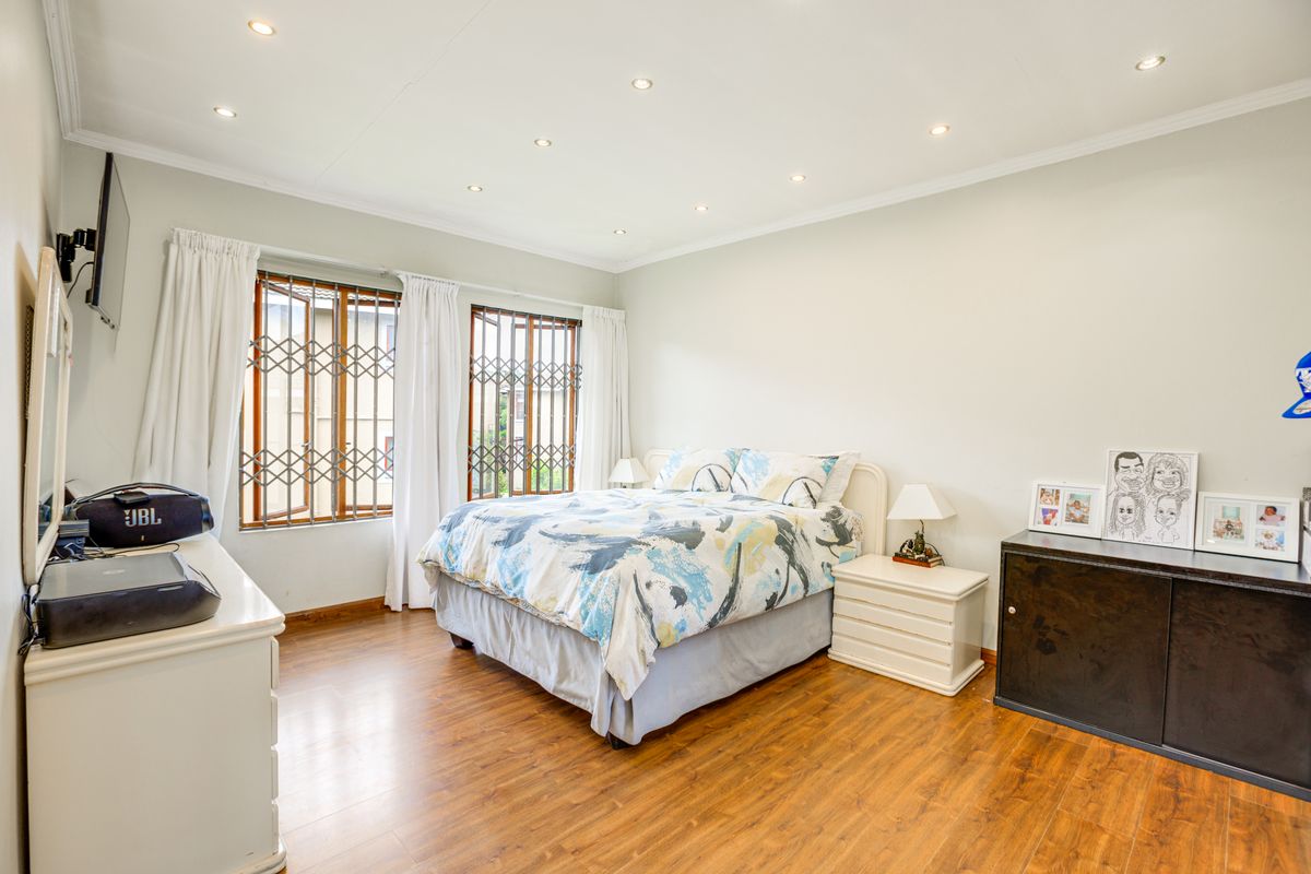 A well-lit bedroom featuring laminate flooring, recessed downlighting, and windows fitted with security gates.
