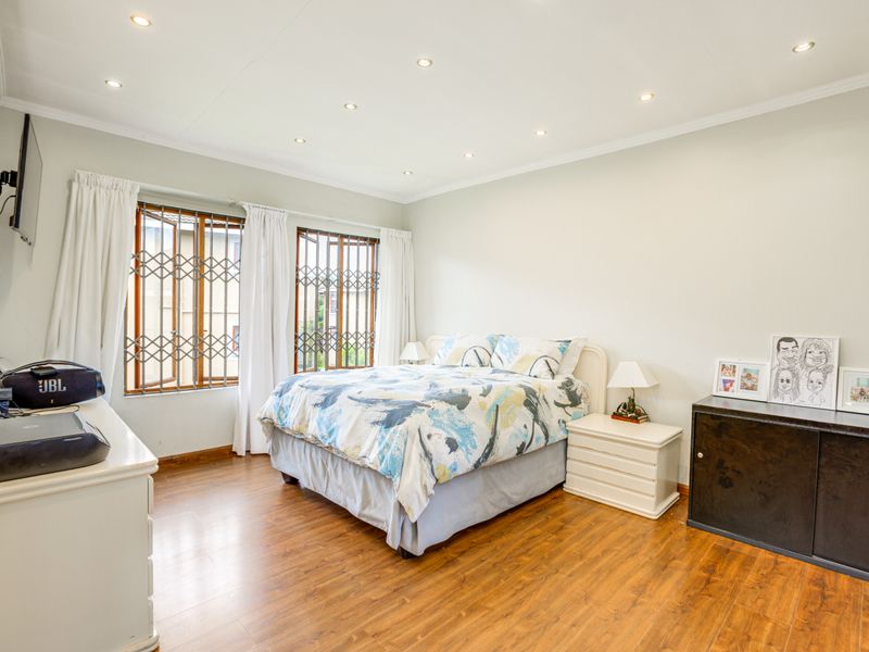 A well-lit bedroom featuring laminate flooring, recessed downlighting, and windows fitted with security gates.