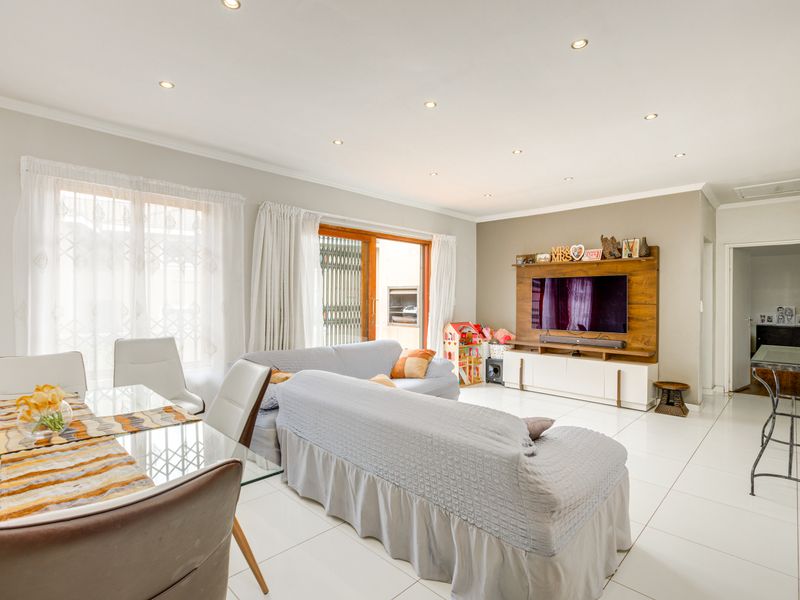 Spacious open-plan living and dining area featuring modern tiled flooring, recessed downlights, and a custom built-in media wall unit with direct patio access.