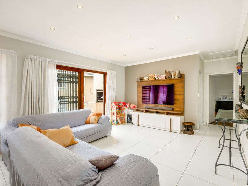 Spacious living room featuring large format floor tiles, recessed downlighting, and a built-in media wall unit with direct access to an outdoor patio area.