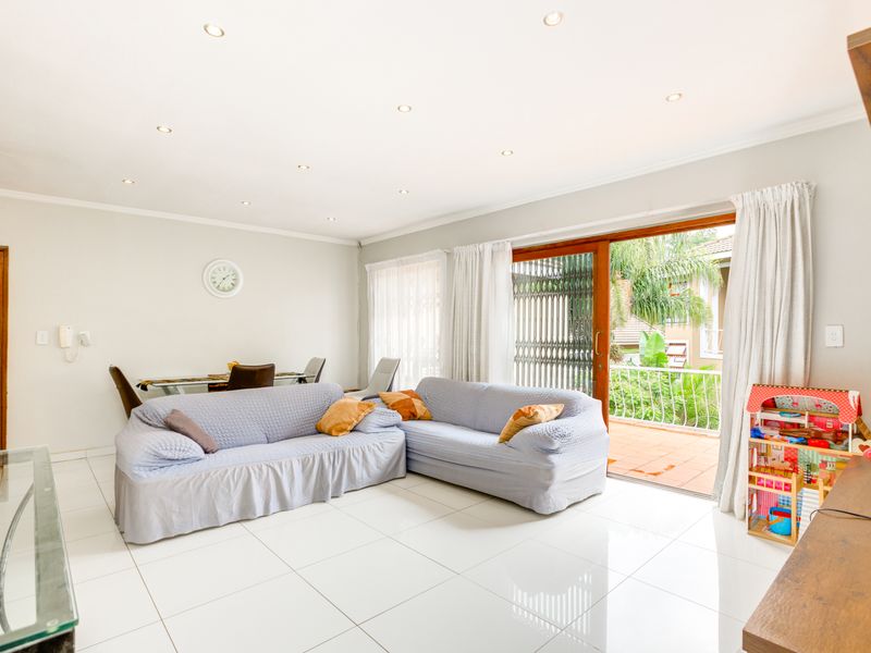 Spacious living room featuring bright tiled flooring, recessed lighting, and a large sliding glass door providing access to an outdoor balcony area.