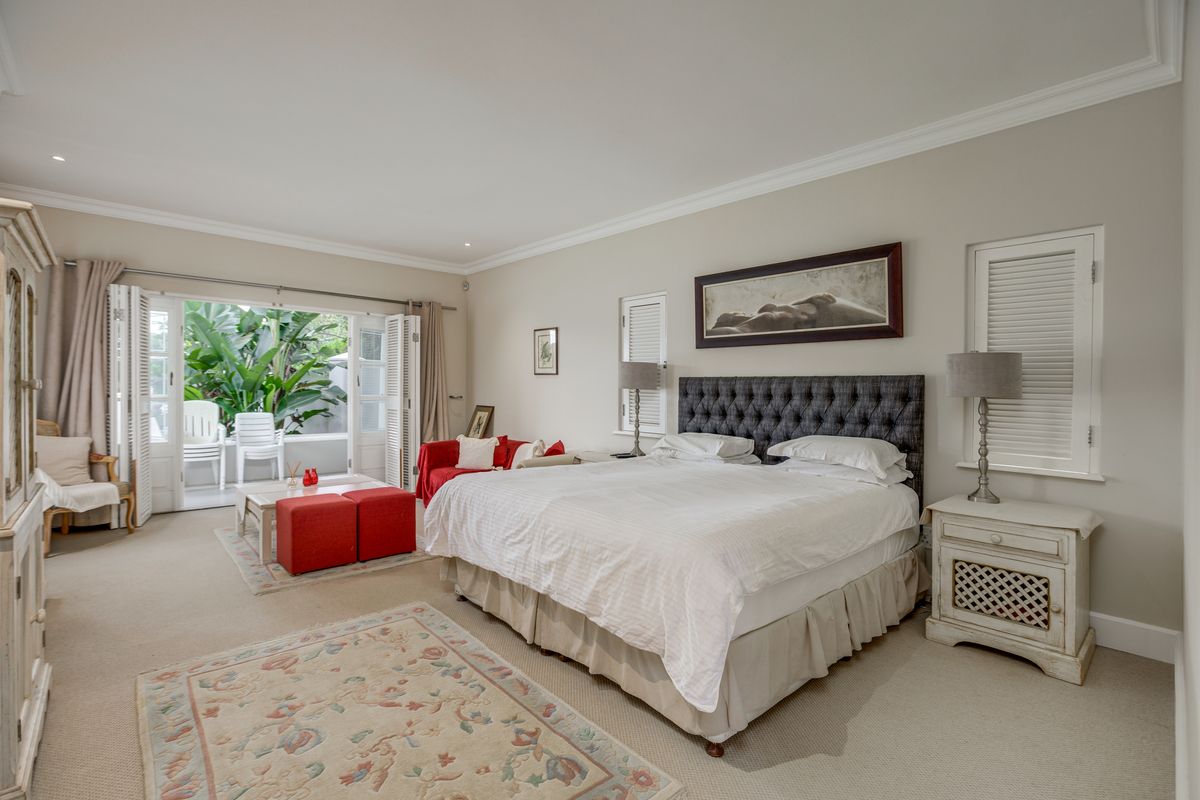 Spacious bedroom featuring neutral carpeting, crown molding, and double doors opening onto a private patio area with lush garden views.