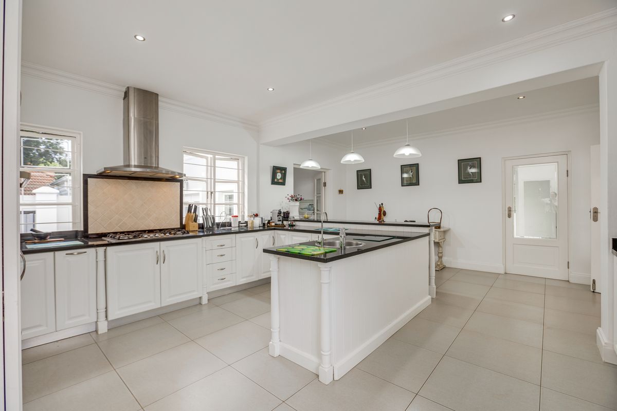 A bright, open-plan kitchen featuring white cabinetry, dark stone countertops, a central island with a sink, and a stainless steel extractor fan.
