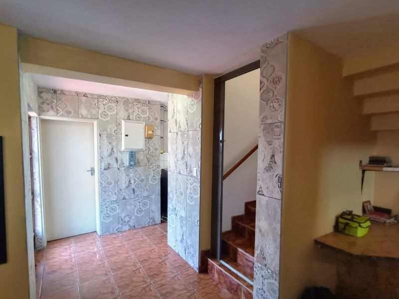 A functional hallway area featuring decorative wall tiles, tiled flooring, and access to an internal staircase with an integrated electrical distribution board.