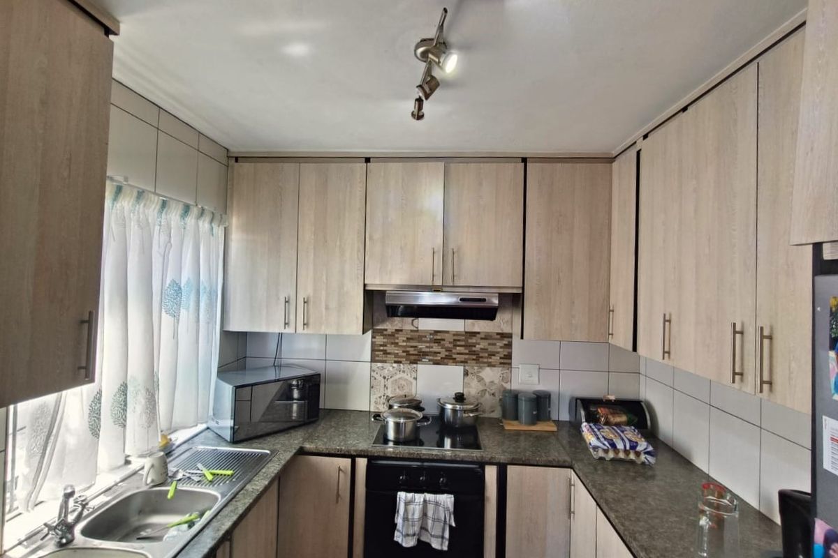A functional kitchen featuring light wood-finish cabinetry, granite-look countertops, a built-in oven with hob, and a double stainless steel sink.