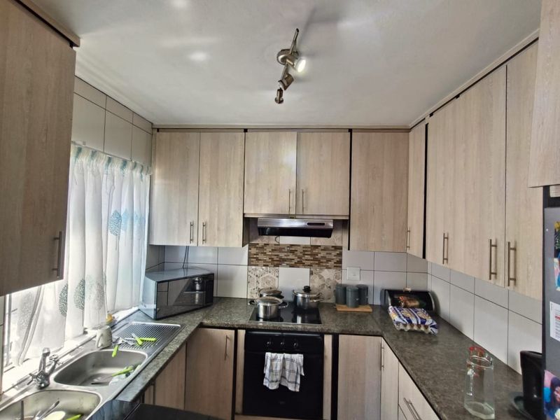 A functional kitchen featuring light wood-finish cabinetry, granite-look countertops, a built-in oven with hob, and a double stainless steel sink.