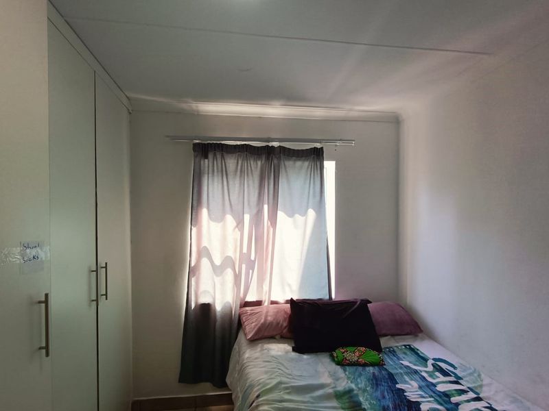 A compact bedroom featuring a built-in wardrobe and a window with a curtain rail, providing functional storage and natural light.