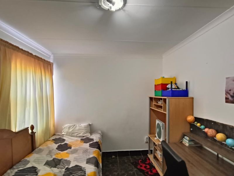 A standard bedroom featuring tiled flooring, a ceiling light fixture, and a window with curtain rails.