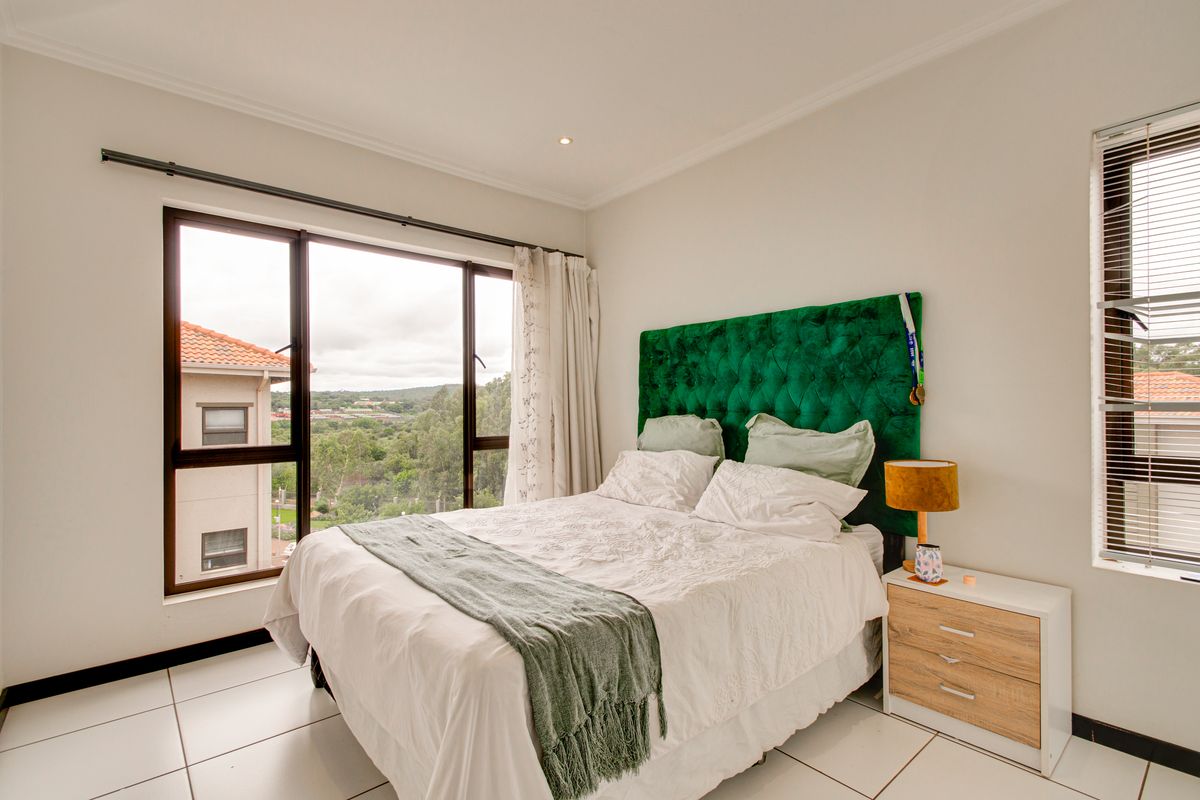 A bright bedroom featuring large windows with scenic views, tiled flooring, and neutral wall finishes.