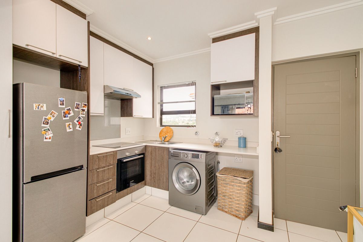 Modern kitchen featuring two-tone cabinetry, integrated oven, hob, extractor fan, and dedicated space for a washing machine with tiled flooring.